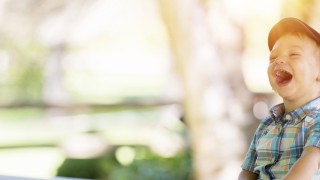 Child laughing, reading book on a bench in a park